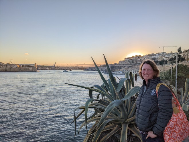 A woman at sunset with a spiky plant and an old walled city behind her
