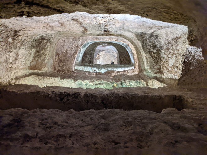 A picture inside the catacombs. You can see tombs, and the light through multiple arches.