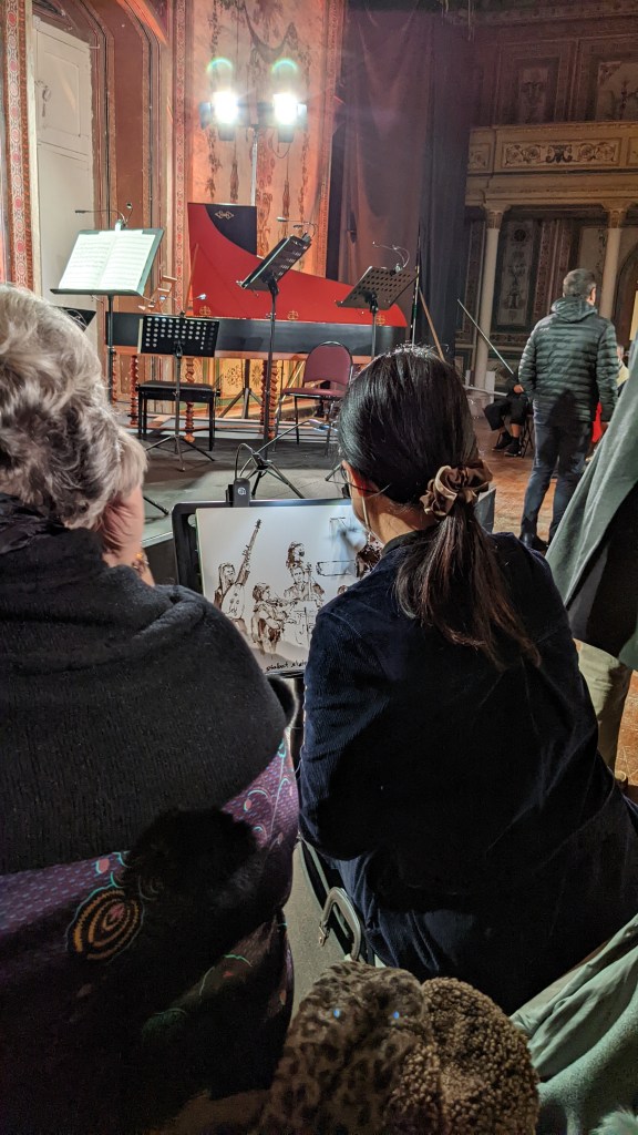 A woman painting a concert scene - you can see her drawing and the harpischold