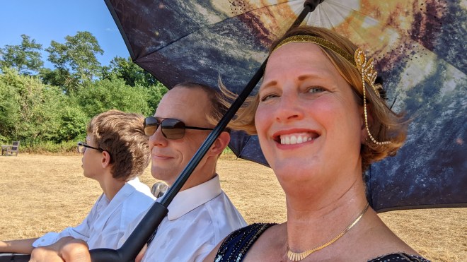 Three people dressed in formal attire underneath an umbrella
