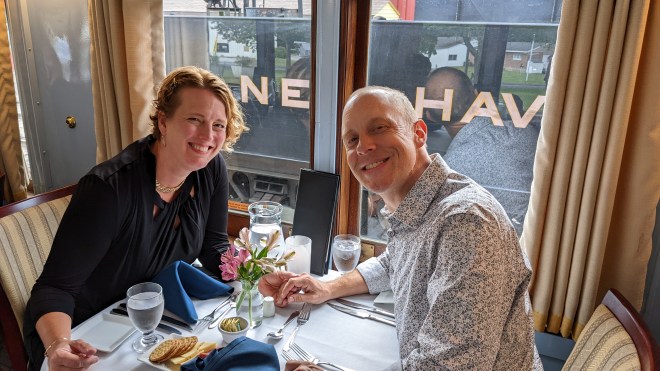 Two people holding hands at a dinner table, with a train behind them.