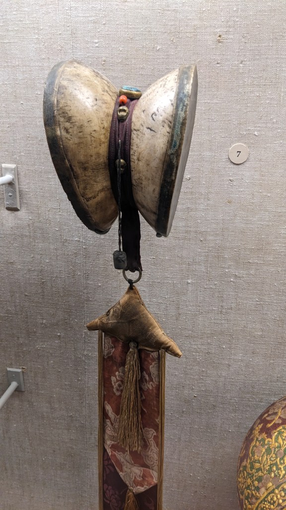 A rattle in a museum case made of the top of two human skulls connected together, with a fabric element hanging off it