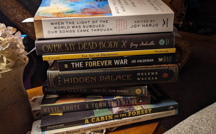 A stack of books by a vase with a flower, in soft lamplight