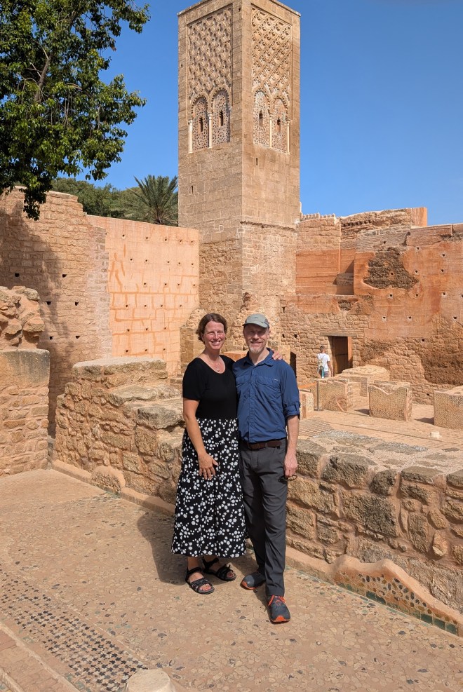 A white couple standing in front of an old yellow brick structure with a bulue sky above