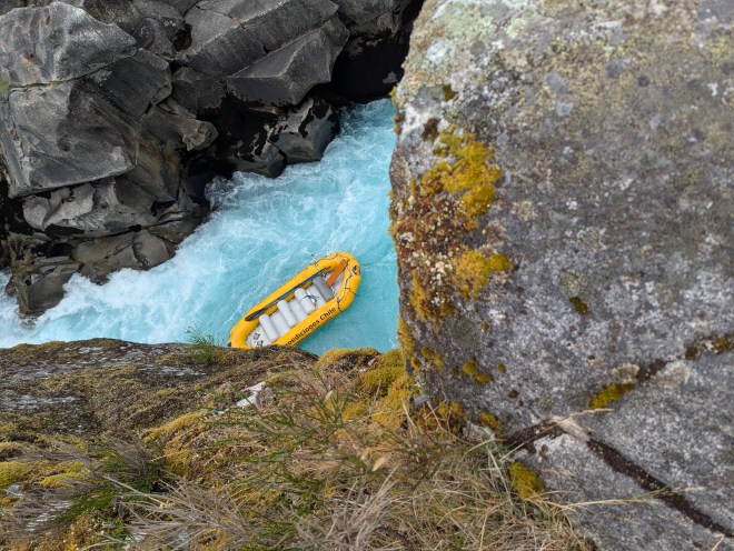 A tiny yellow raft far below in shockingly blue waters, surrounded by all sides by mossy granite boulders