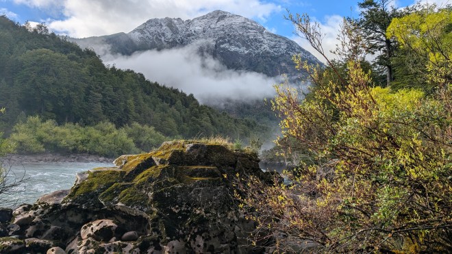 A mountain wreathed in mist with a river and a rock
